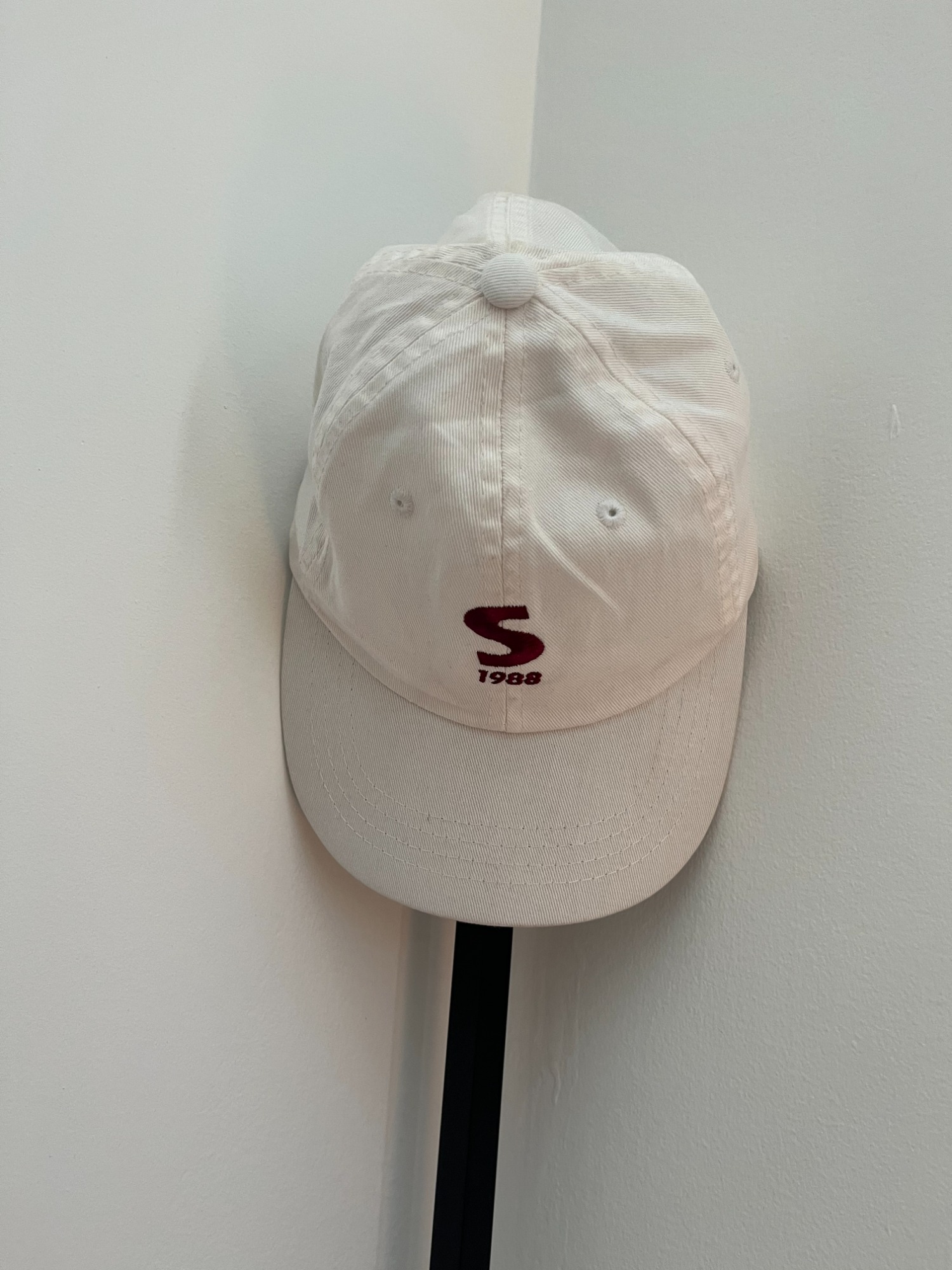 SUEDE1988 white cap hanging on a wall hook, front view