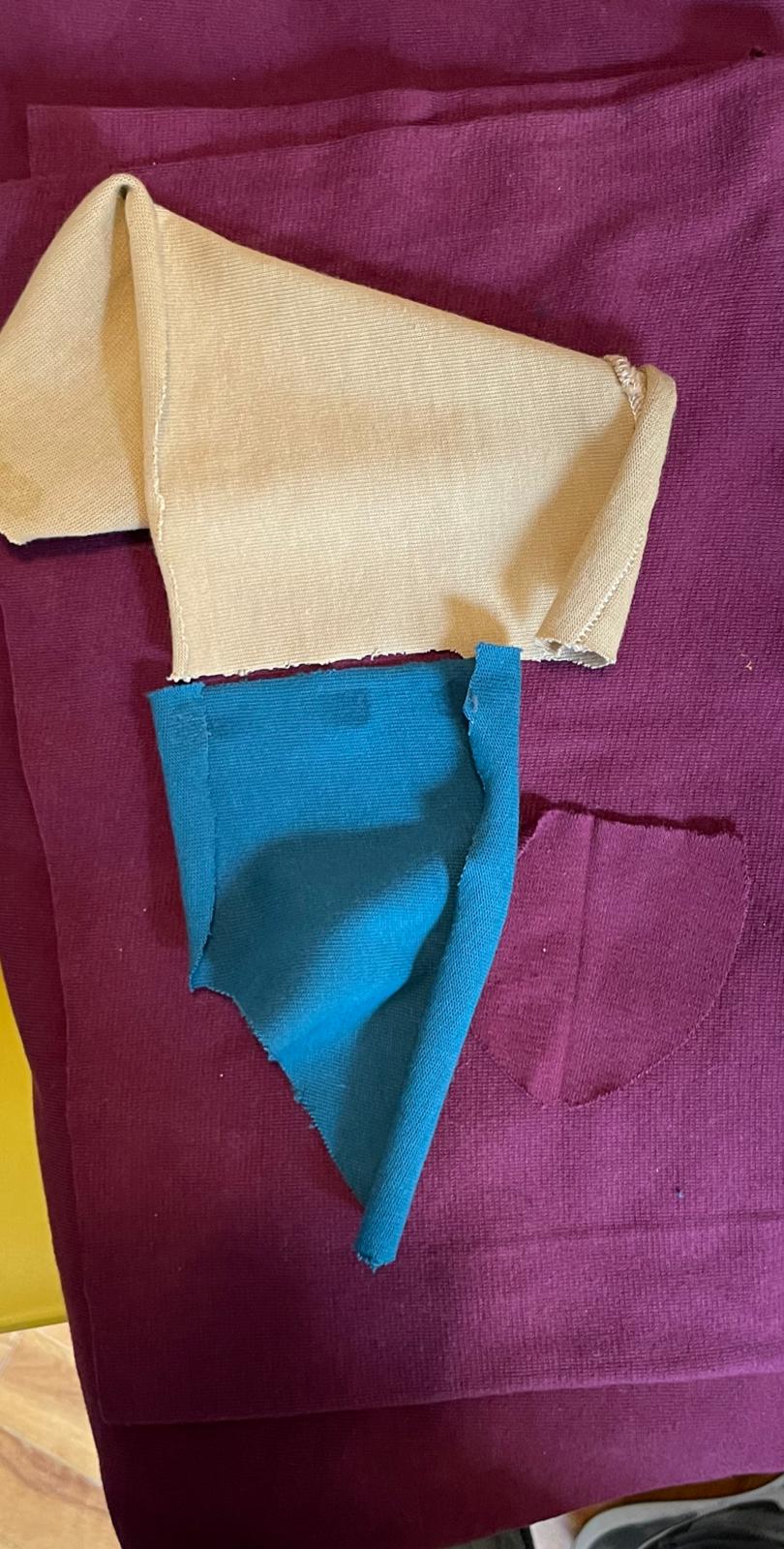 Cut panels for a maroon garment — pocket, collar and trim pieces laid out